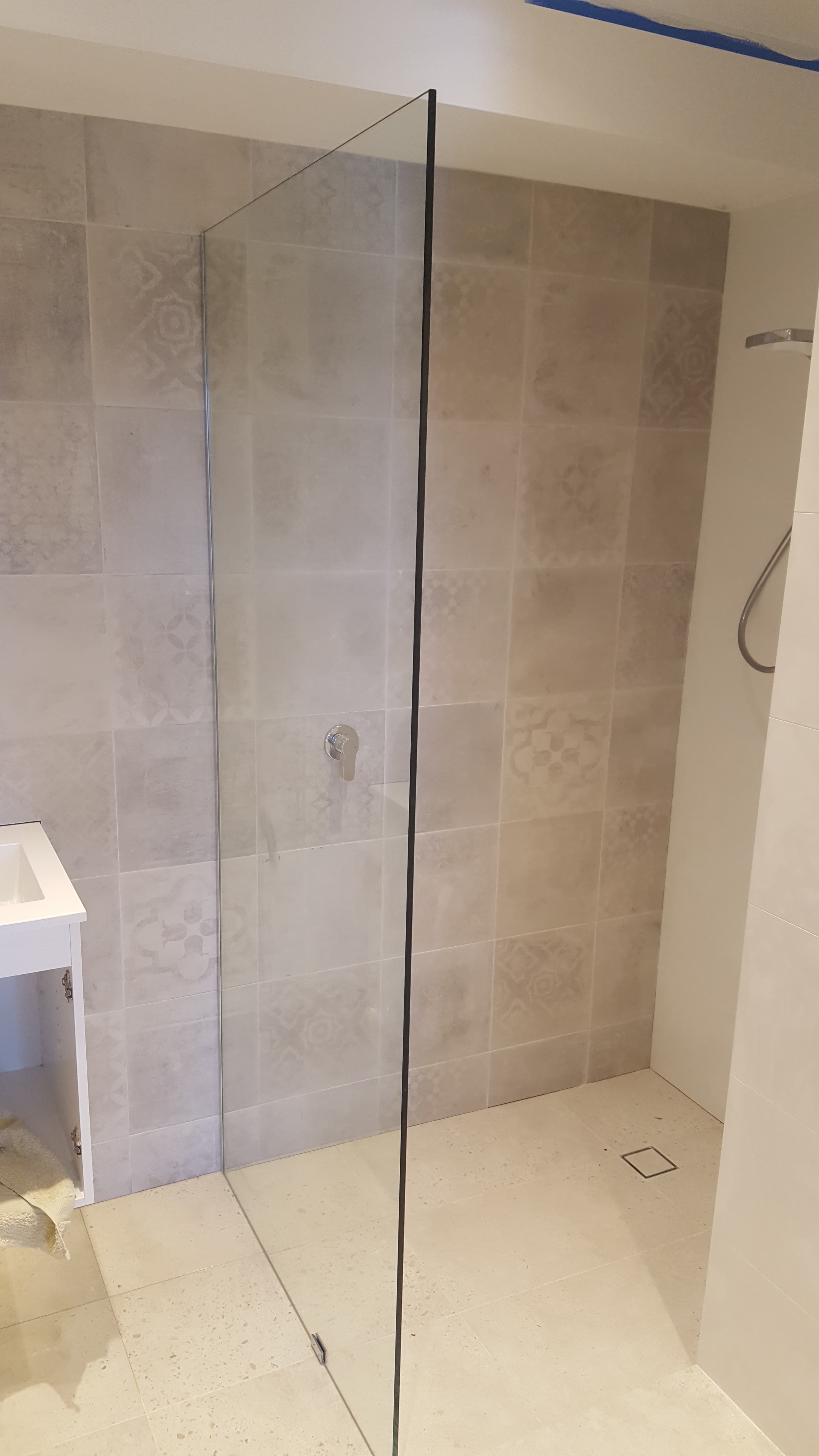 Walk-in shower with a frameless glass screen, light grey patterned tiles, and a chrome mixer.