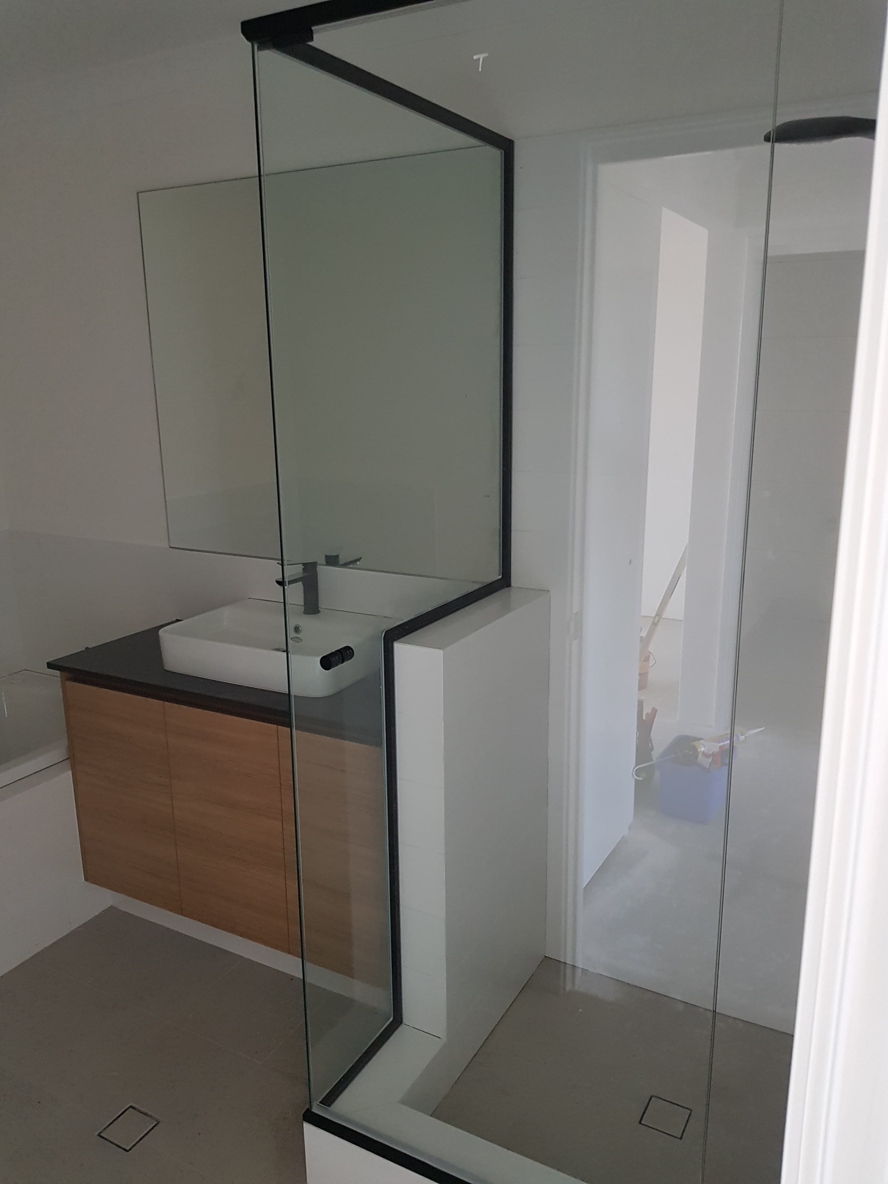 Modern bathroom with a wooden vanity, white vessel sink, and black-framed glass shower screen.