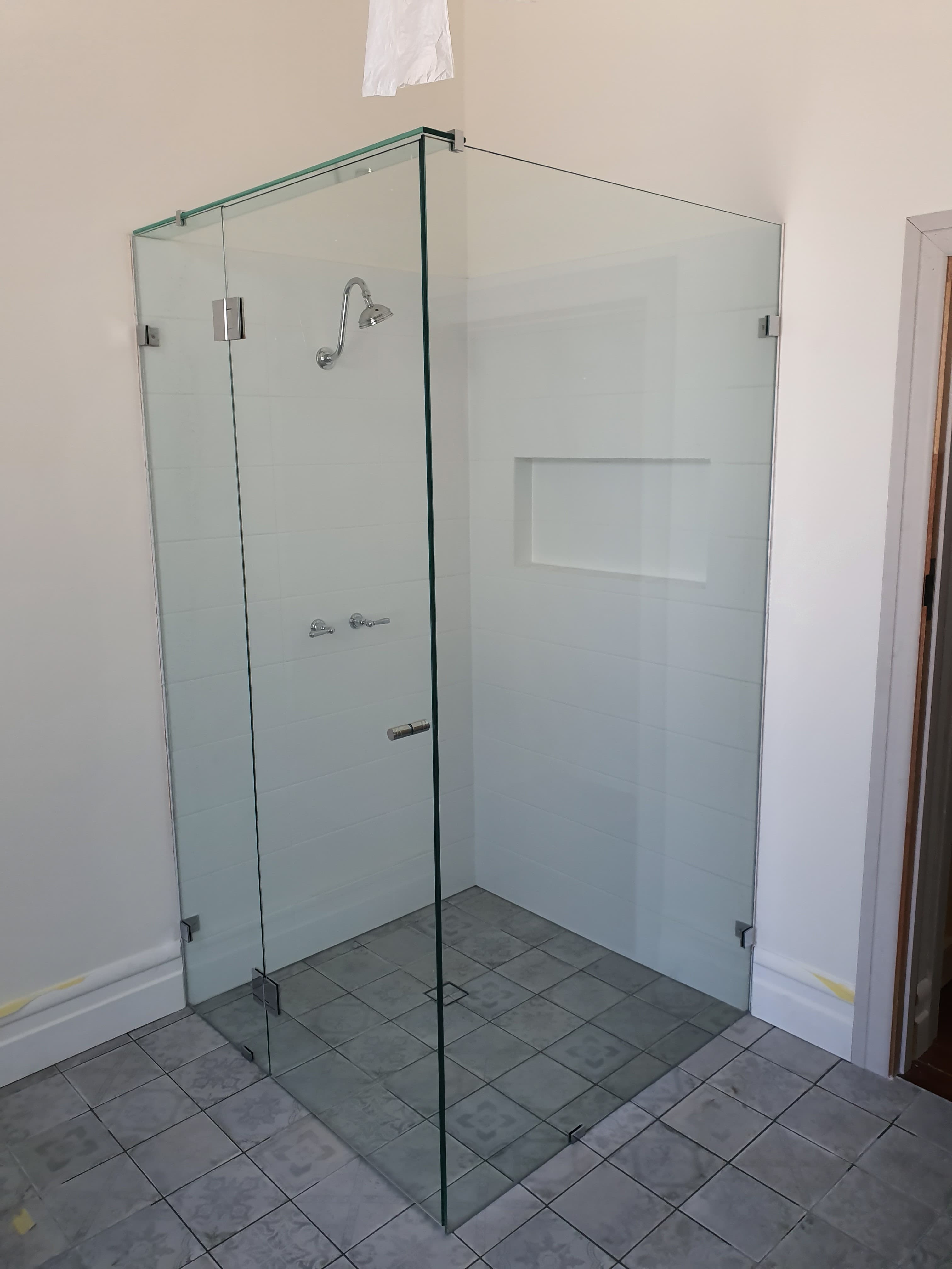 Frameless glass shower enclosure with chrome fixtures, white tiled walls, and a gray patterned floor.