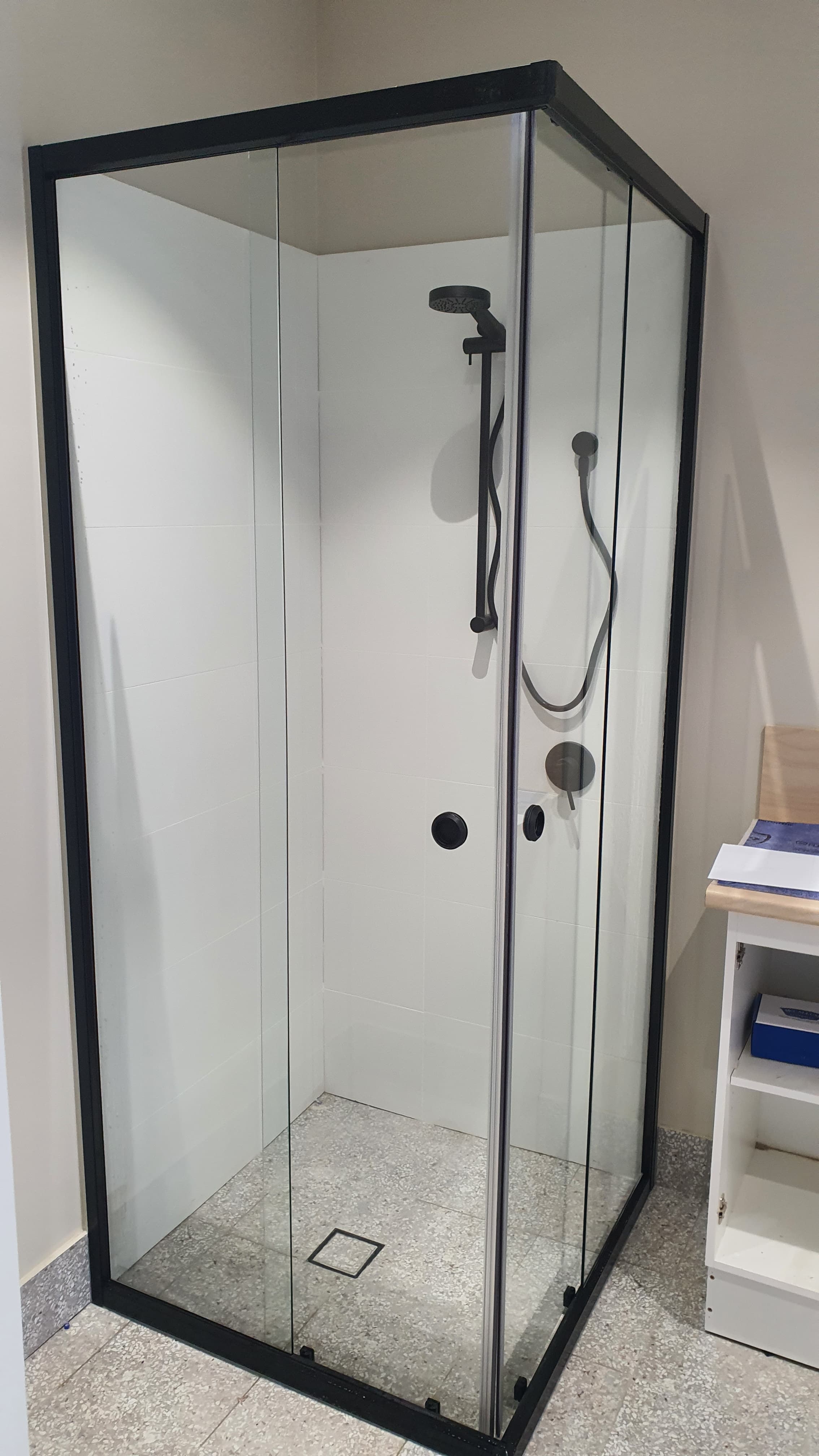Modern corner shower featuring a black frame, glass panels, white tiles, and black shower hardware.