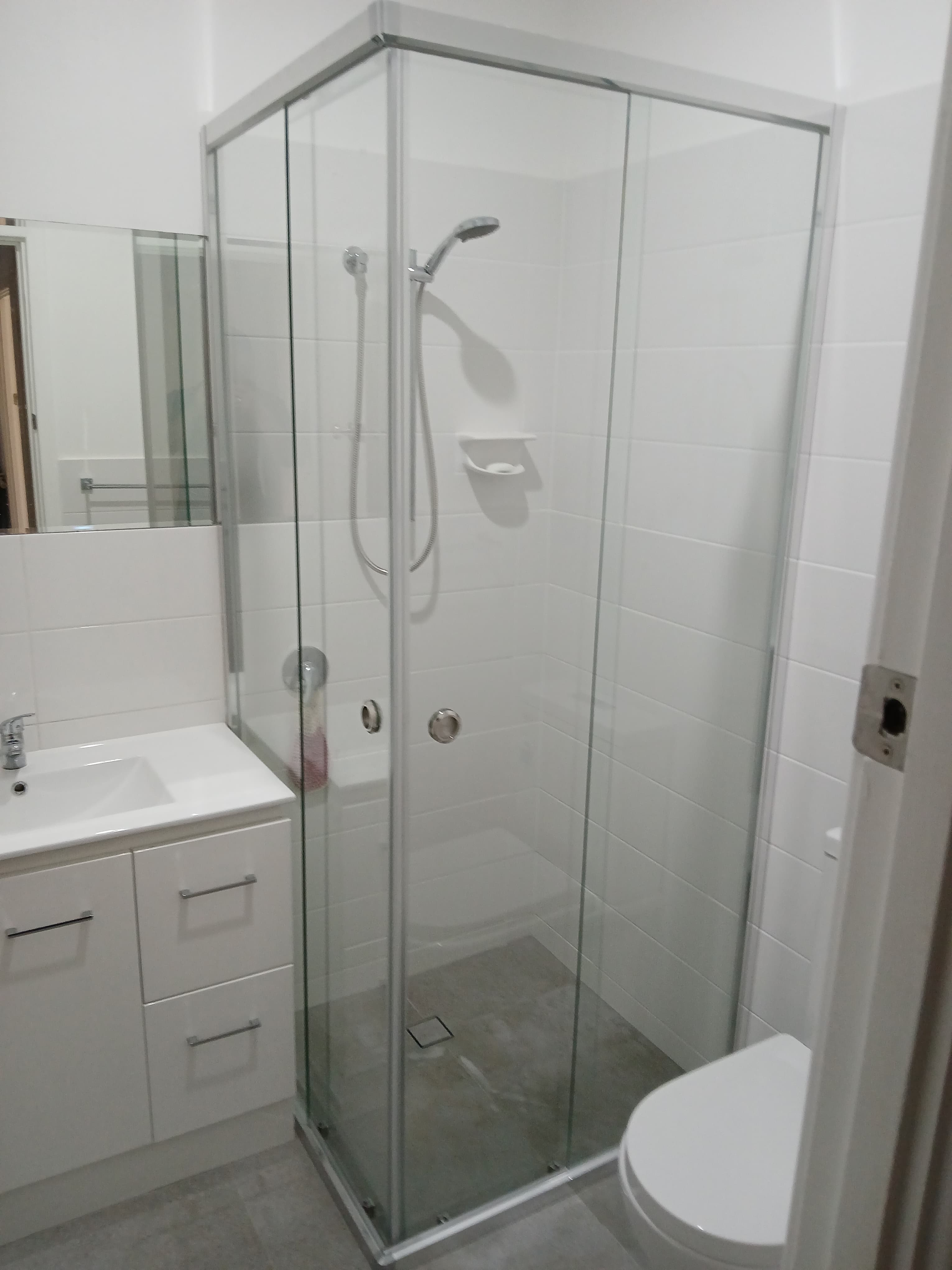 Modern white bathroom featuring a glass corner shower, white vanity, and grey tiled floor.