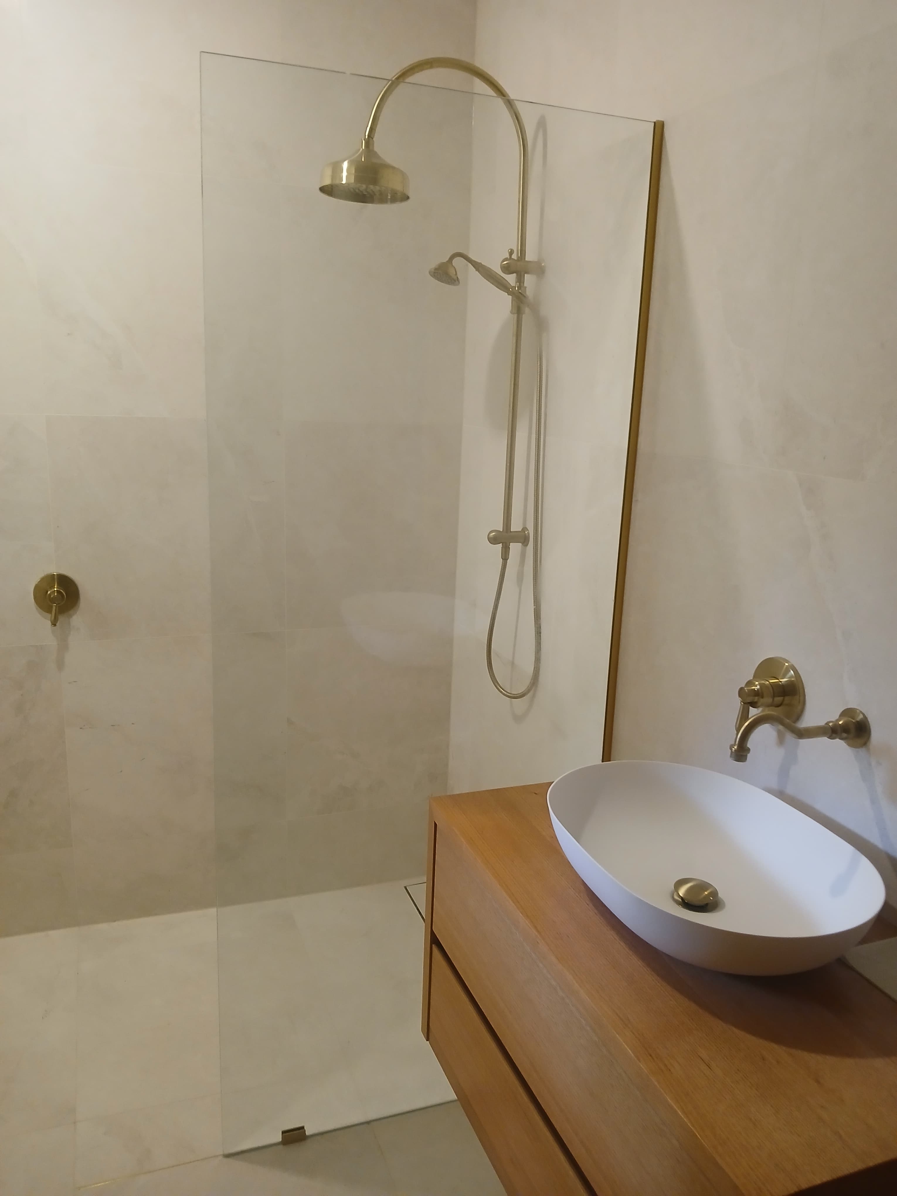 Elegant bathroom with gold shower fixtures, glass partition, and white vessel sink on wooden vanity.