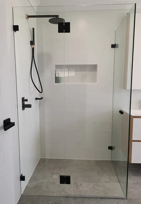 Modern frameless glass shower with matte black fixtures, white tiled walls, and a built-in niche.